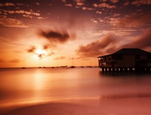 silhouette of house in ocean water during sunset thumbnail