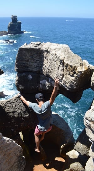 man in gray gray t-shirt and pink shorts climbing on rocks near sea thumbnail