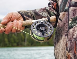 man holding fishing rod near body of water during daytime thumbnail