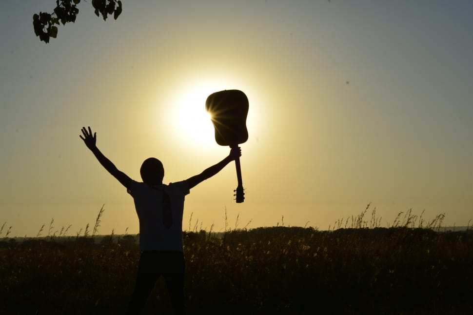 silhouette of man raising both hands carrying guitar preview