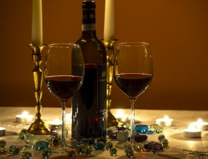 photo of wine bottle with two wine glasses with wine inside surrounded with marble toys and tealight candle thumbnail