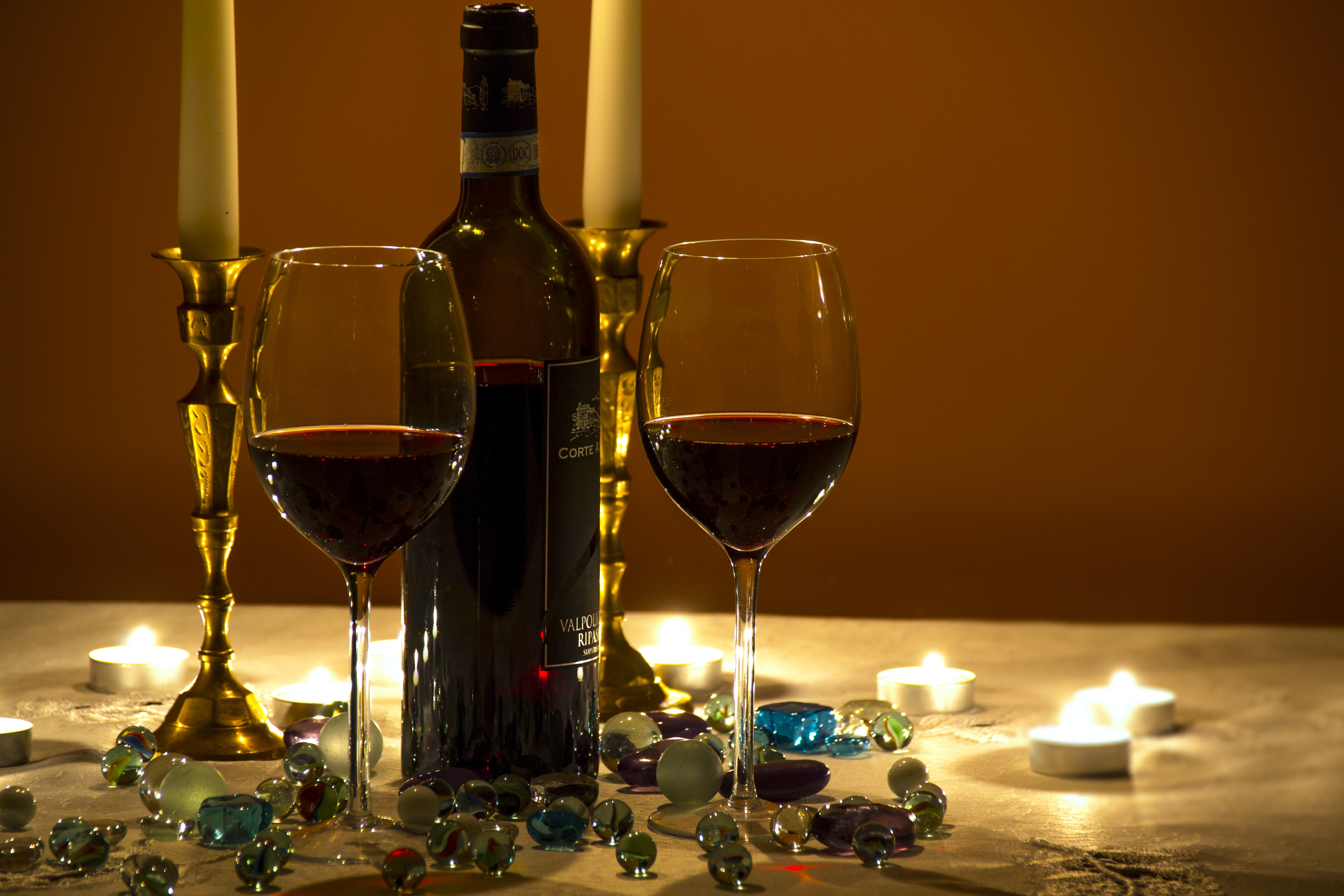 photo of wine bottle with two wine glasses with wine inside surrounded with marble toys and tealight candle