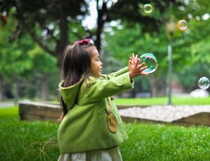 girl in green hoodie touching bubbles during daytime thumbnail