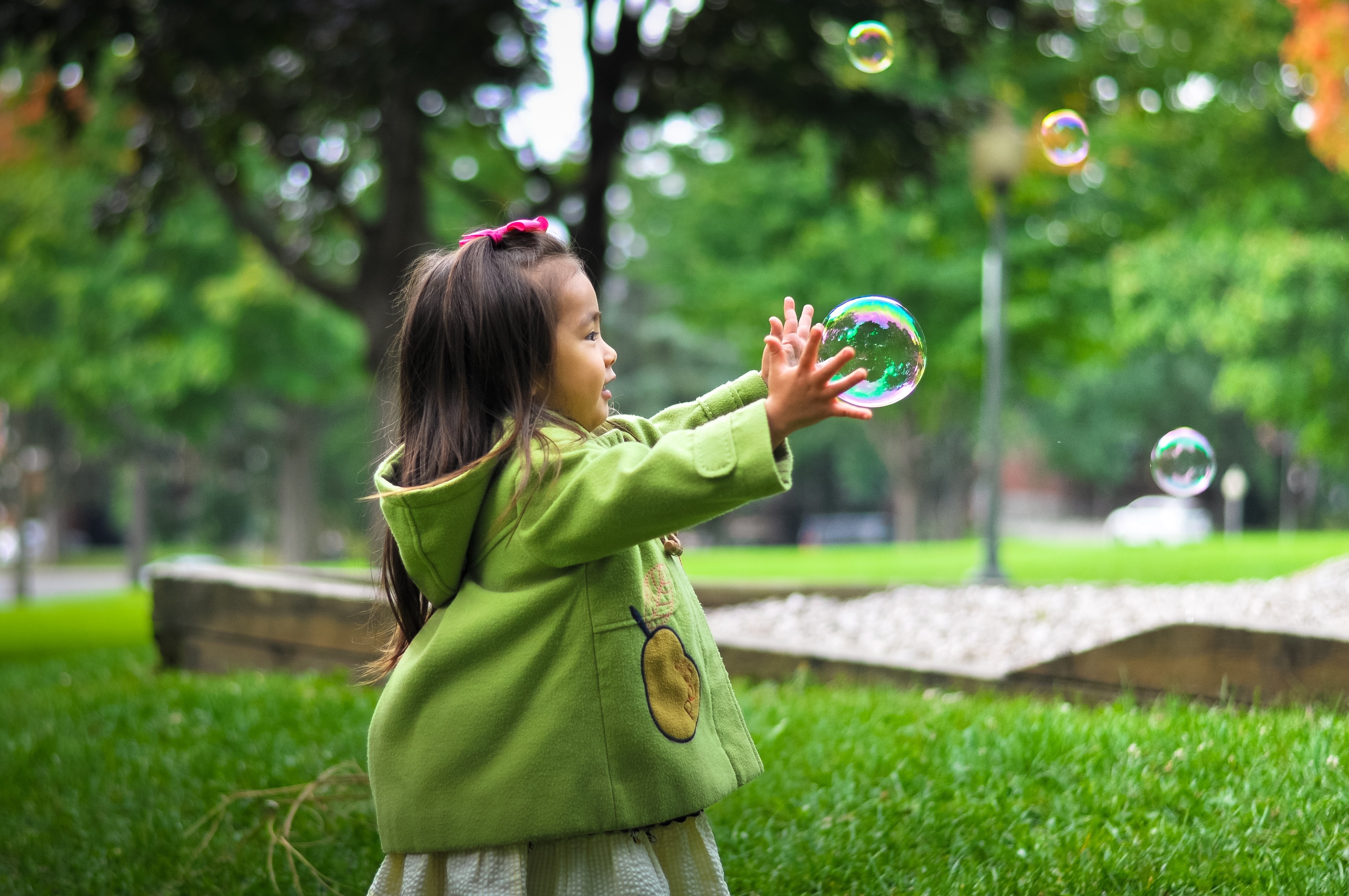 girl in green hoodie touching bubbles during daytime