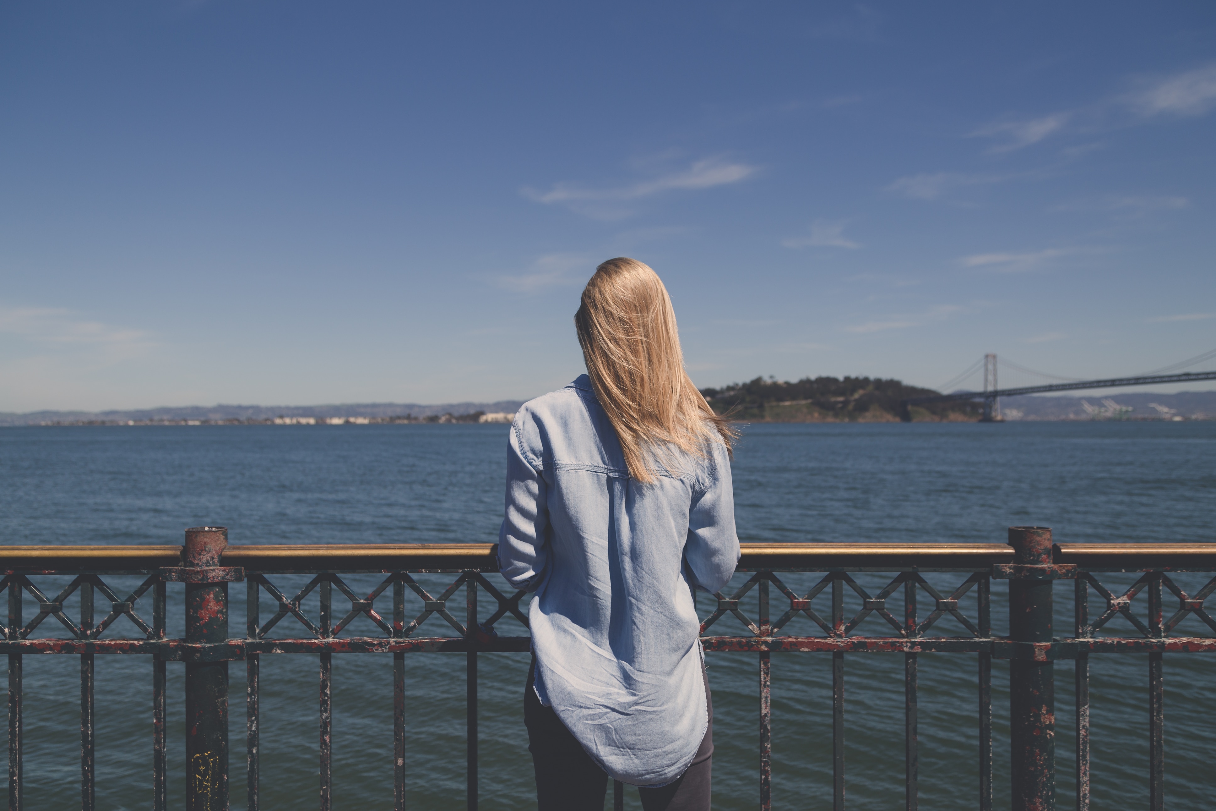 blonde haired woman in blue denim top standing near body of water during daytime