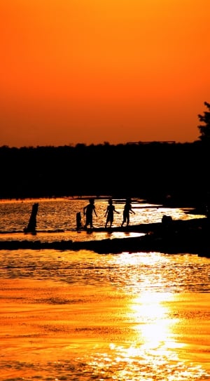 silhouette of children on body of water during sunset thumbnail