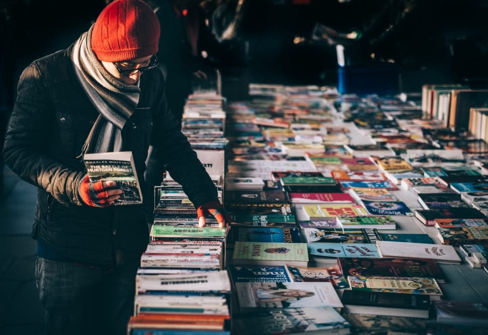 man in black coat and red knit cap wearing sunglasses holding book photo preview