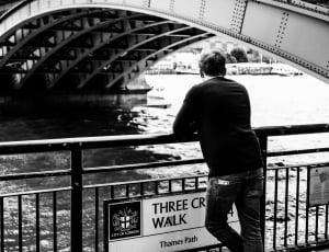 man leaning on river fence grayscale photo thumbnail