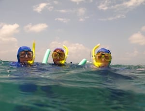 three person floating on sea wearing wetsuit and snorkels during daytime thumbnail