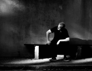 grayscale photo of man sitting on bench thumbnail