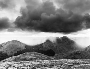 grayscale photography of clouds under mountain during daytime thumbnail