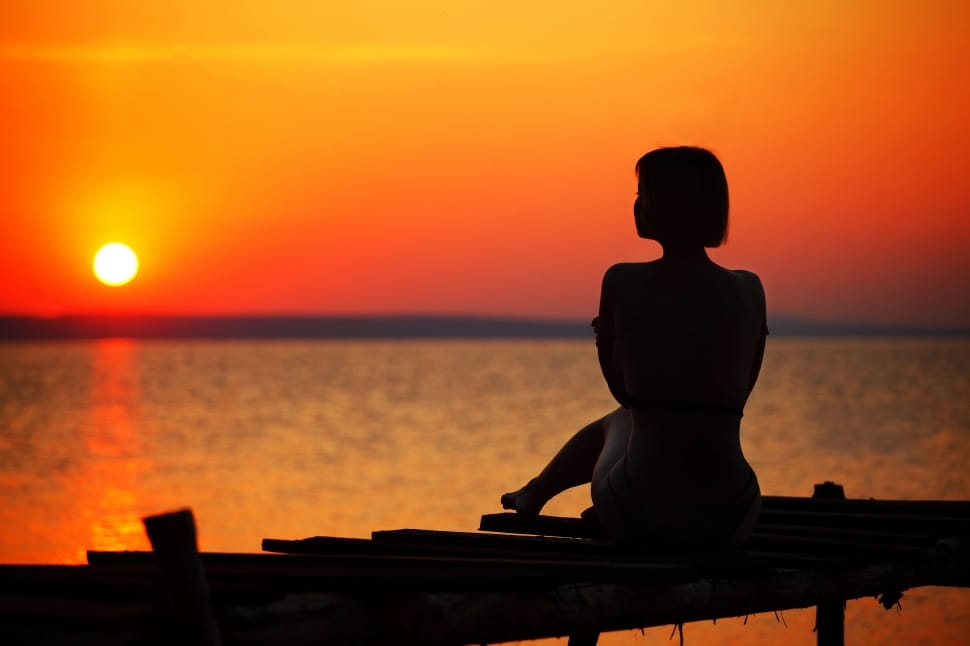 woman sitting on dock during sunset preview