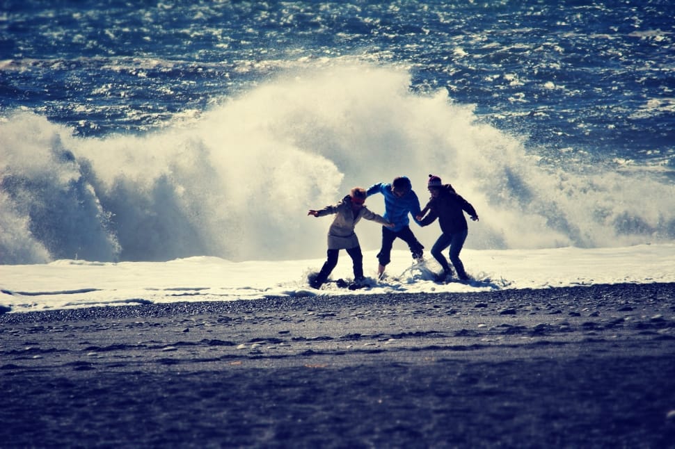 photo of three person standing in shoreline near a wave preview