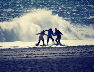 photo of three person standing in shoreline near a wave thumbnail