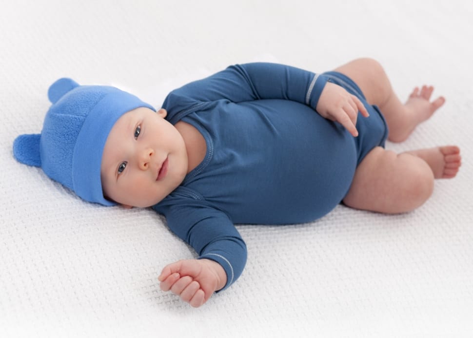 photo of baby wearing blue hat and gray onesie lying on bed preview