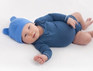 photo of baby wearing blue hat and gray onesie lying on bed thumbnail