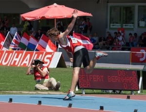 man in red jersey top, black cycling and white shoes on a track field thumbnail