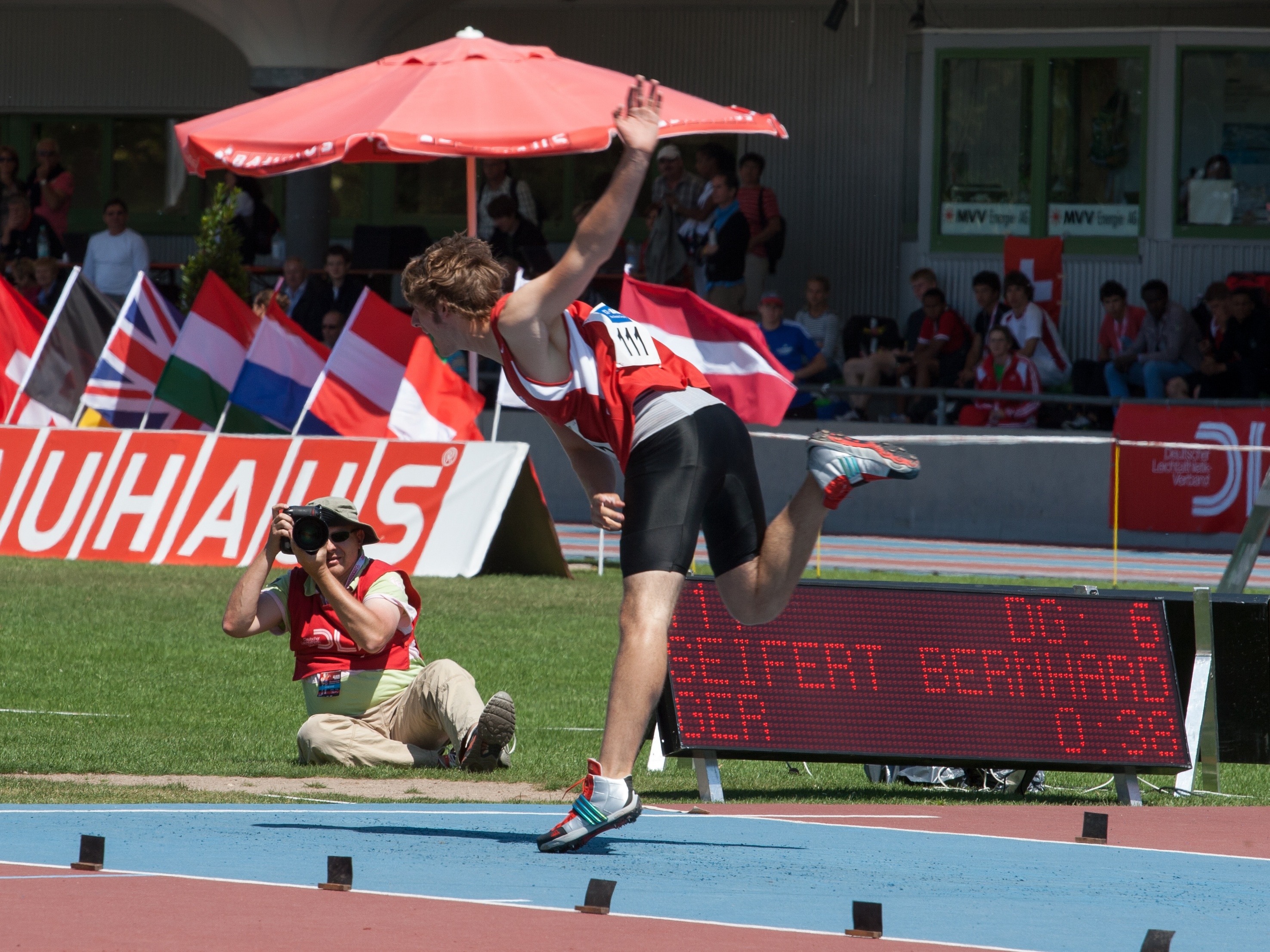 man in red jersey top, black cycling and white shoes on a track field