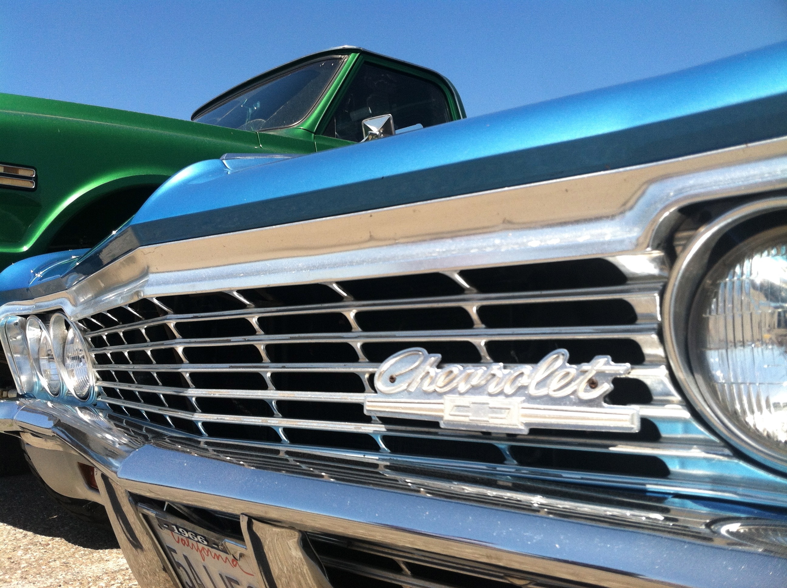 Chevrolet car beside green pickup truck under blue clear sky