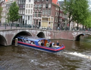 group of people riding on blue and red speedboat in the middle of the city near beige city concrete bridge thumbnail