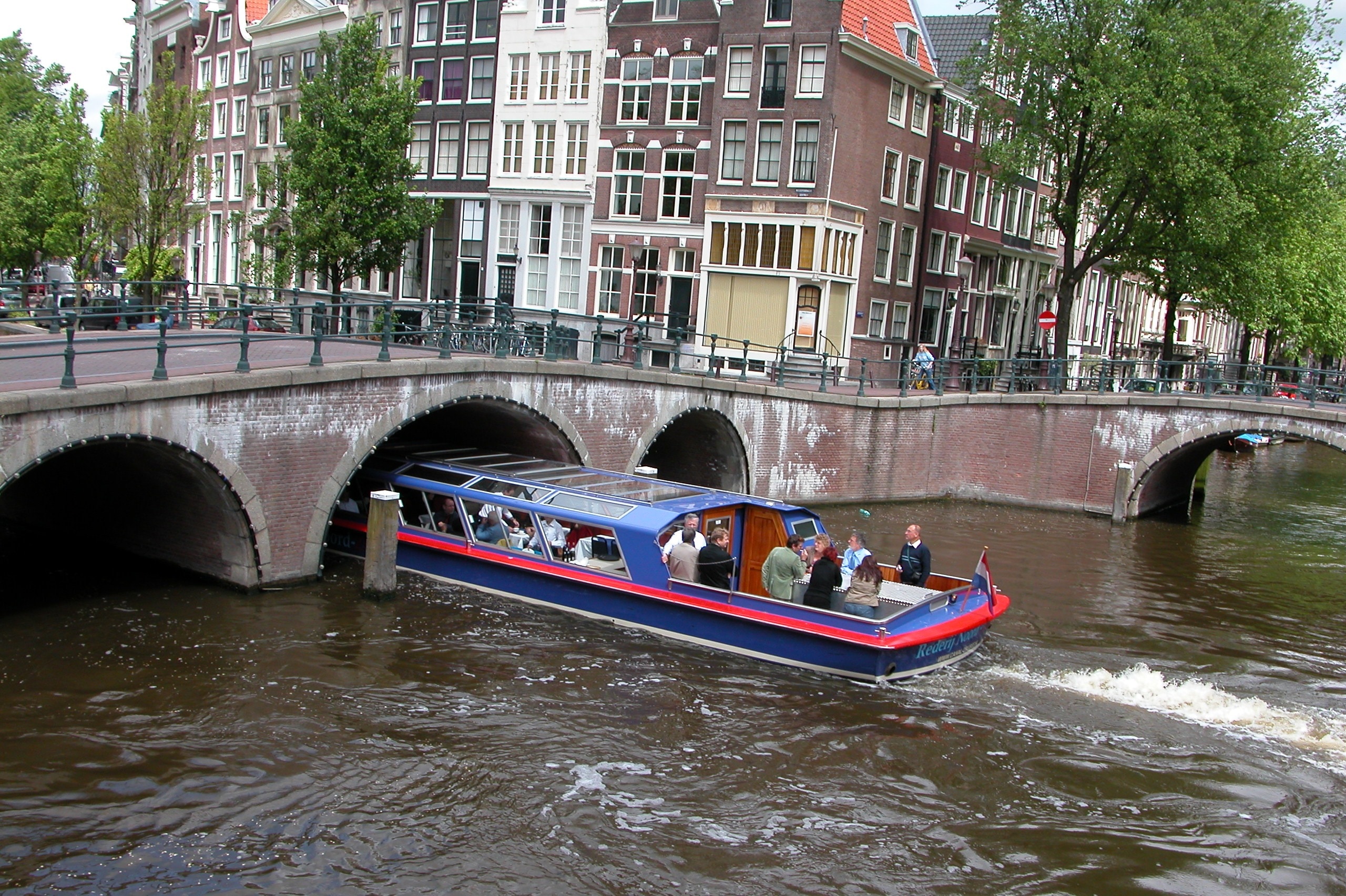 group of people riding on blue and red speedboat in the middle of the city near beige city concrete bridge