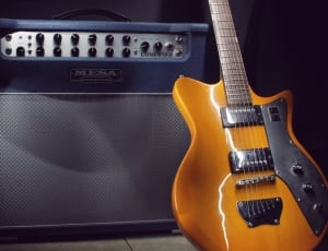 orange electric guitar near gray mena guitar amplifier thumbnail