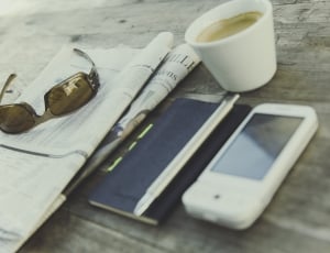white smartphone beside click pen, sunglasses and ceramic cup thumbnail