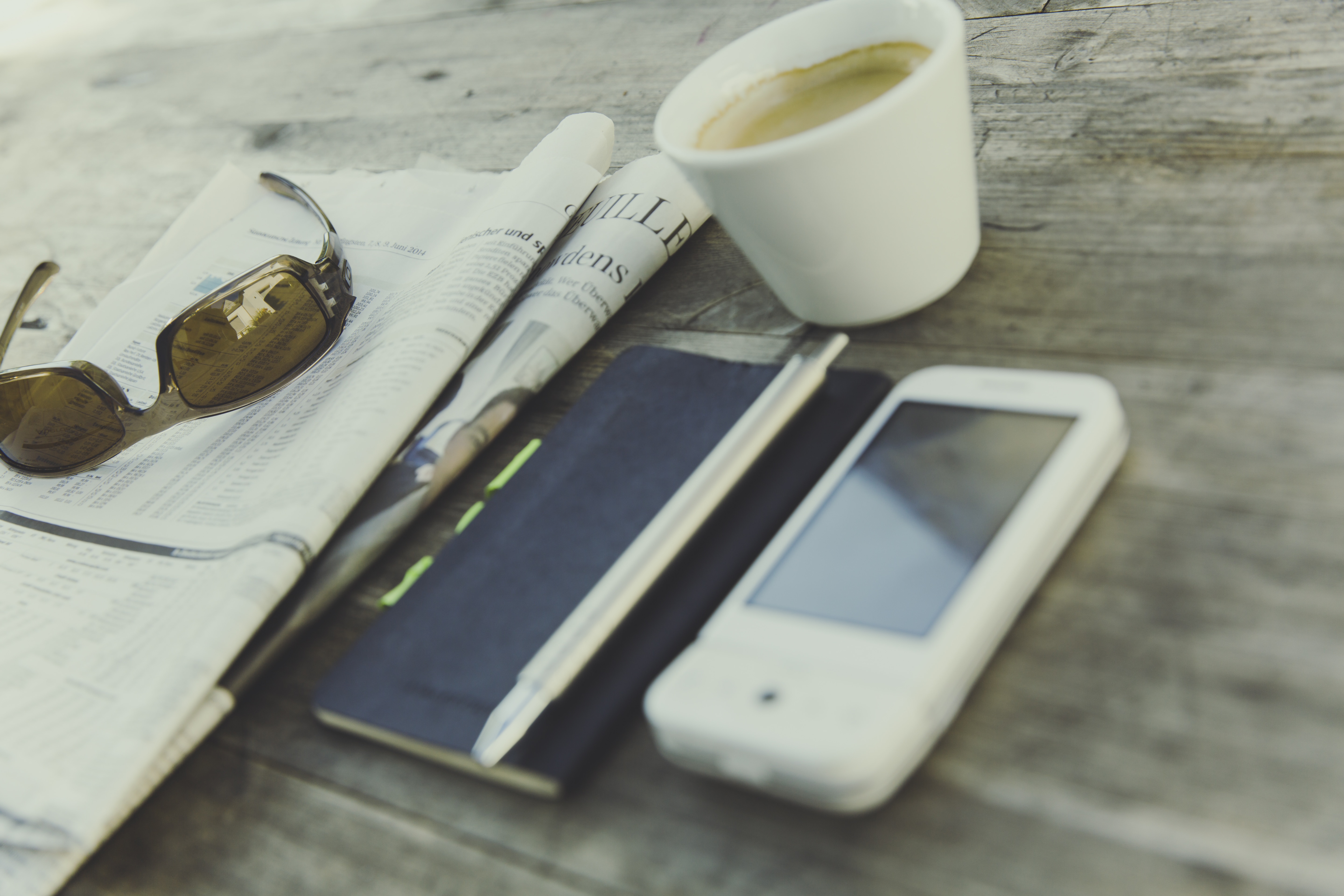 white smartphone beside click pen, sunglasses and ceramic cup