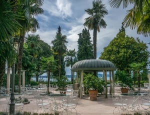 white patio tables and chairs and green tall trees during daytime thumbnail