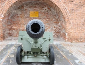 green and black cannon near brown brick walled building thumbnail