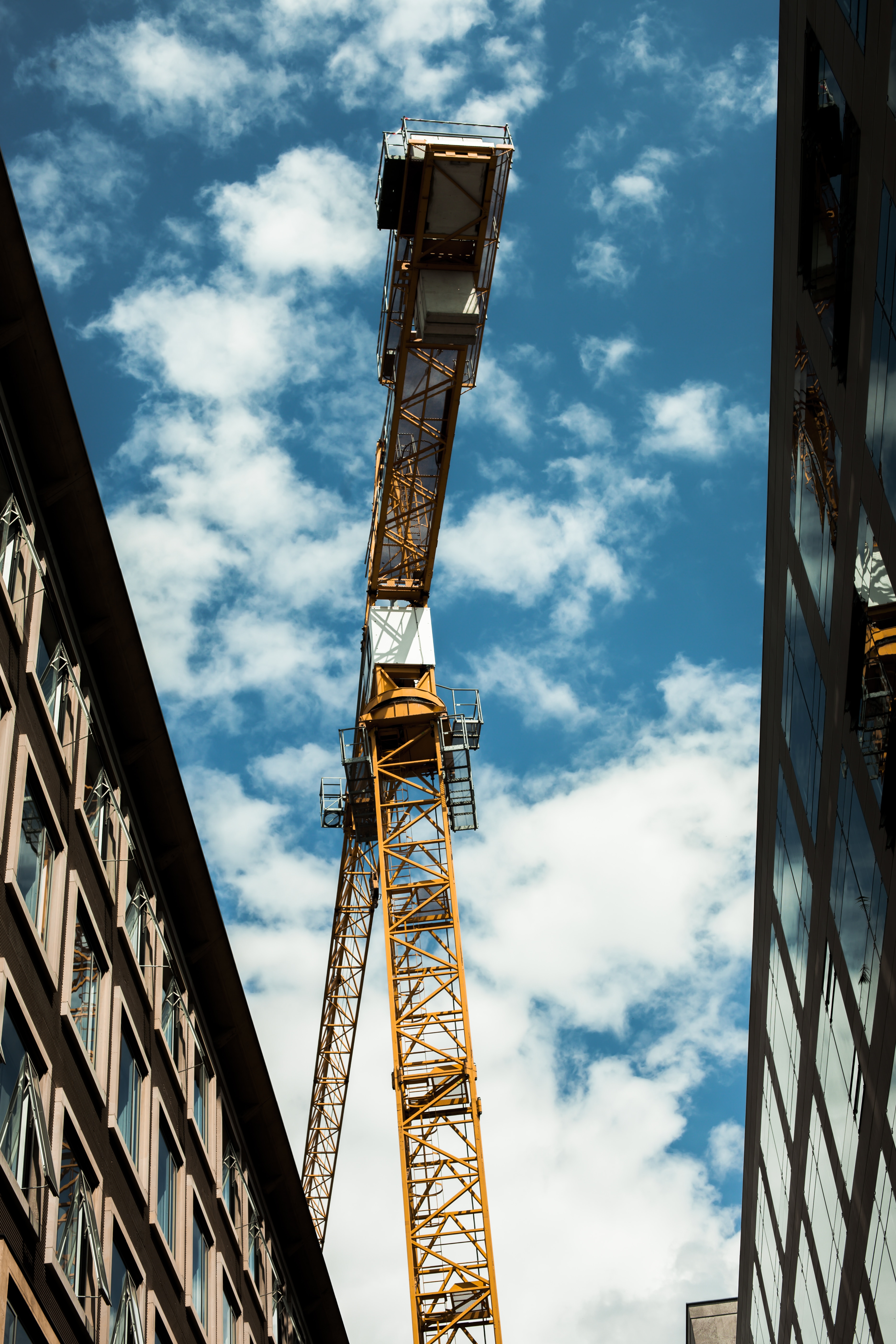 low angle photo of yellow crane in between two high rise buildings under blue sky and white clouds