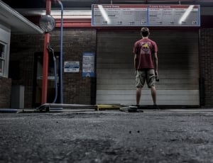 man in red shirt and pair of brown shorts standing on steel shutter door outdoors during nighttime thumbnail