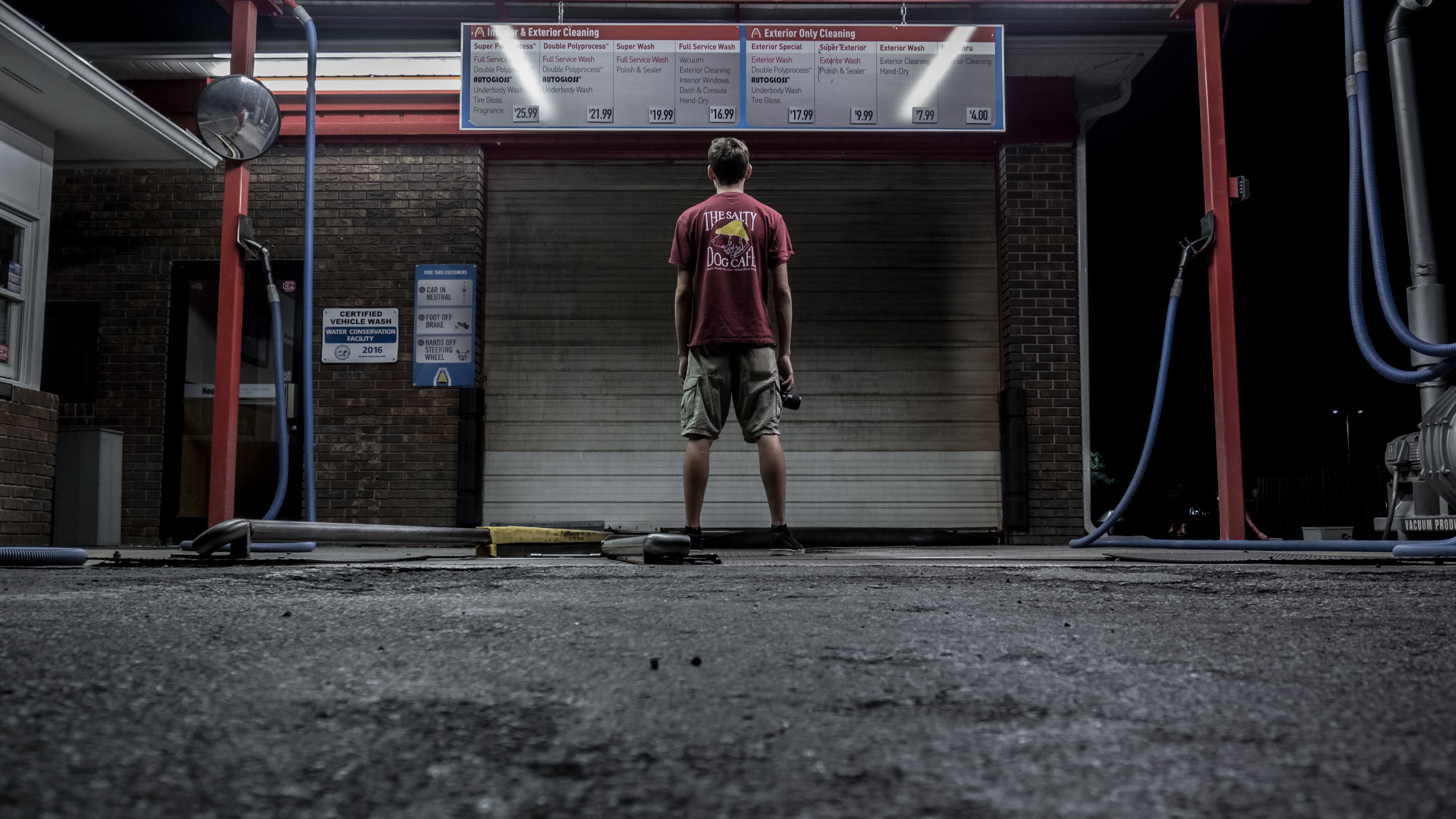man in red shirt and pair of brown shorts standing on steel shutter door outdoors during nighttime