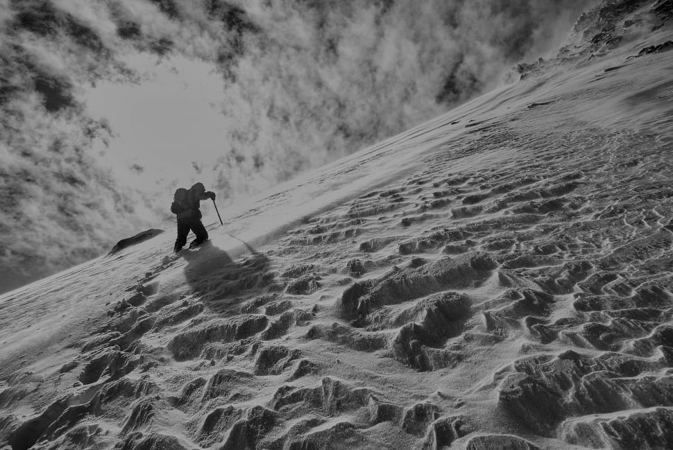 greyscale photography of a man hiking on a snow covered mountain during daytime preview