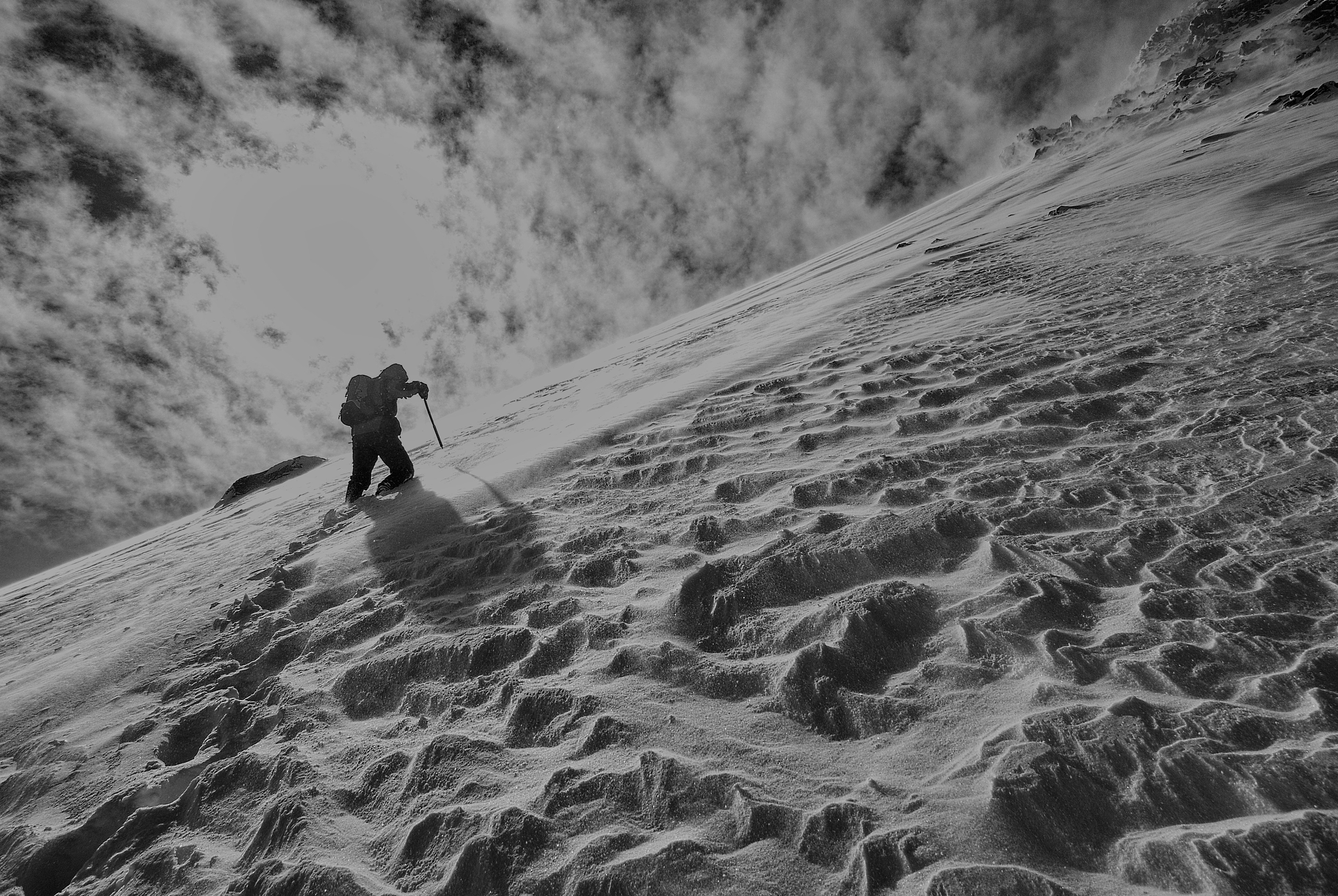 greyscale photography of a man hiking on a snow covered mountain during daytime