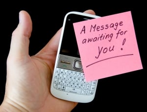 person holding qwerty phone with a message awaiting for you sticky note thumbnail