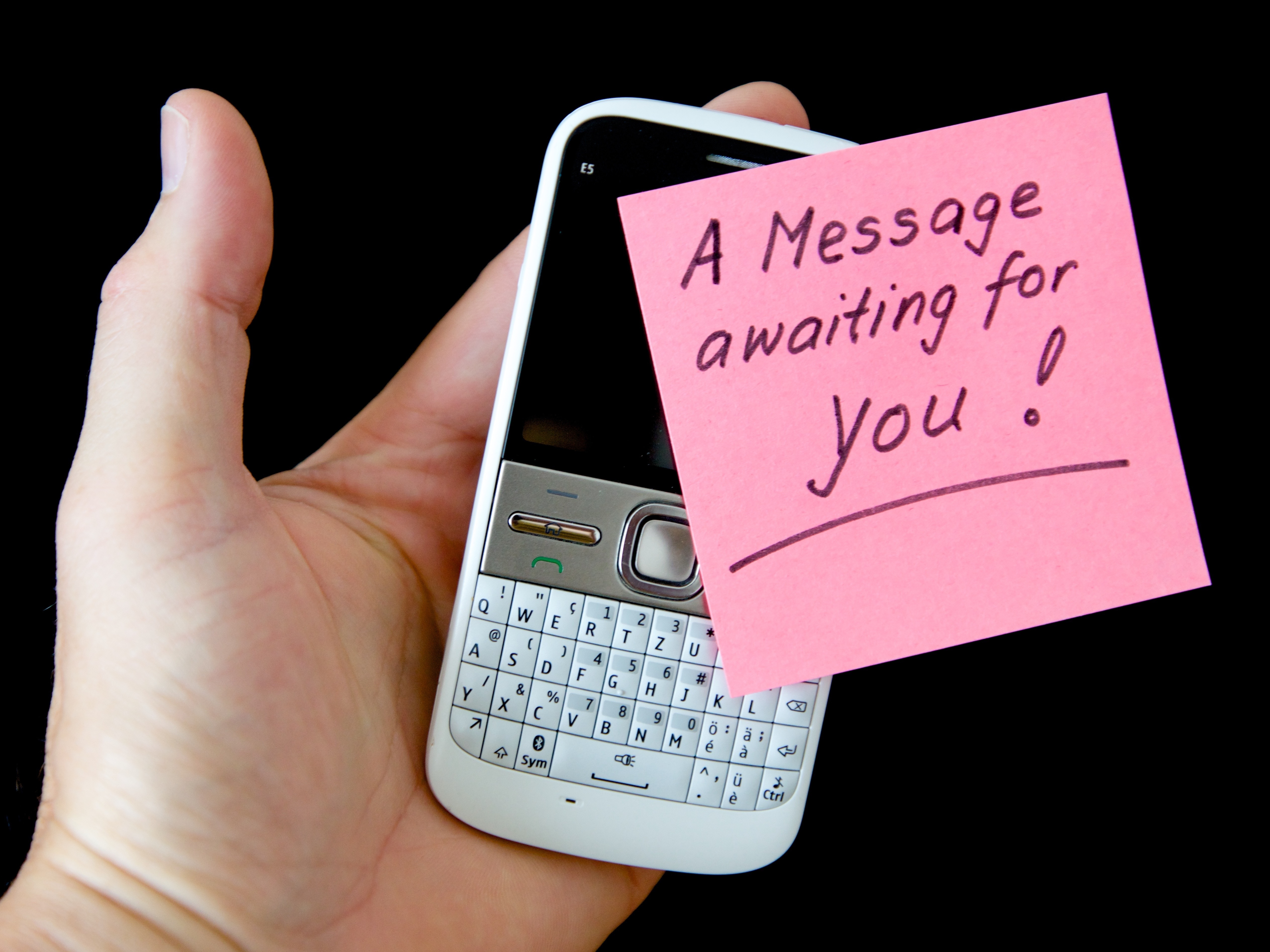person holding qwerty phone with a message awaiting for you sticky note