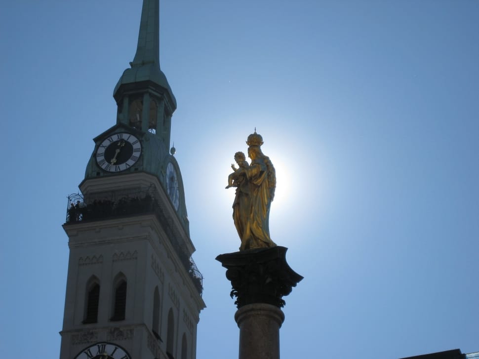 woman carrying baby statue near tower with analog clock under blue sky preview