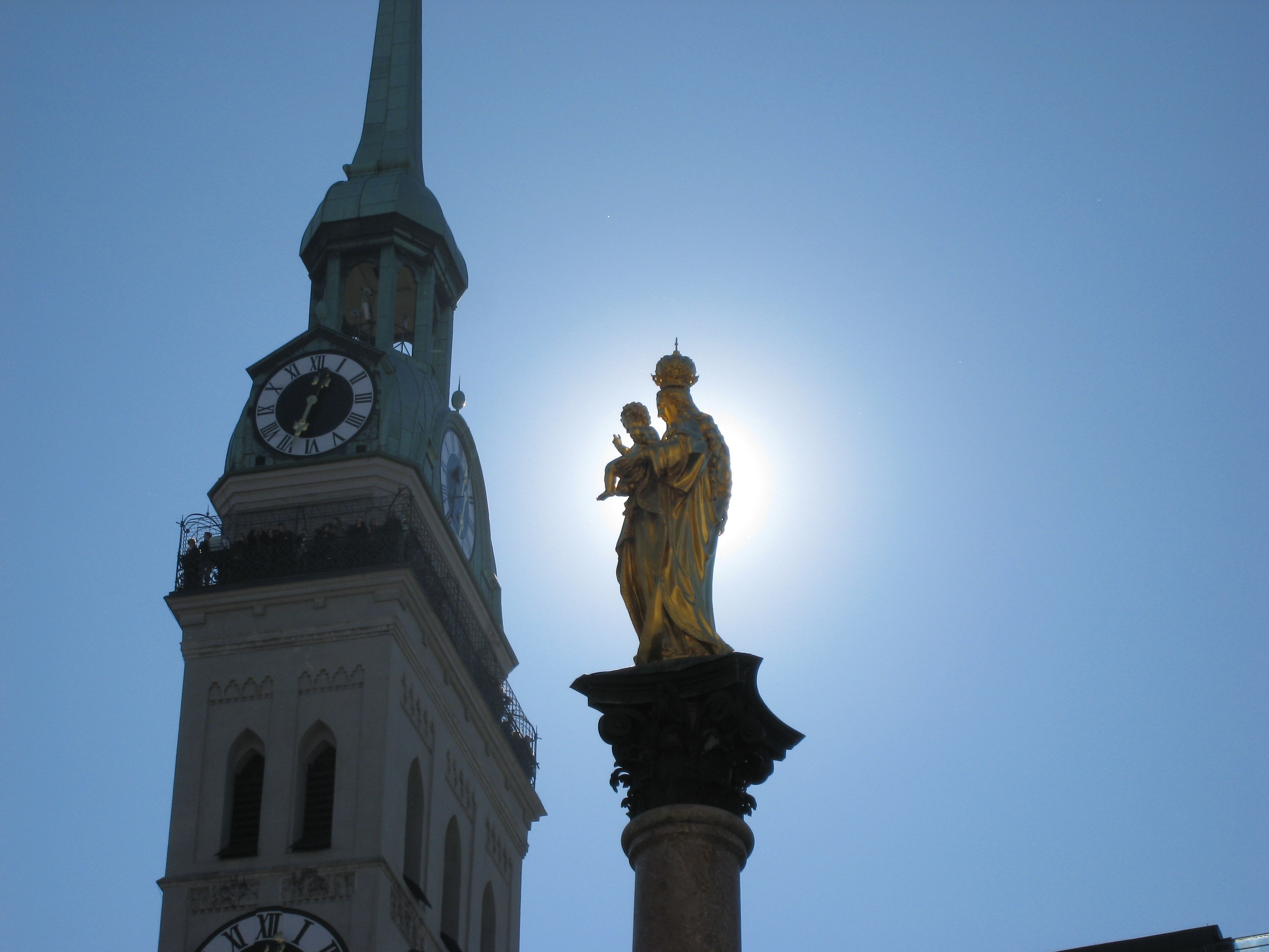 woman carrying baby statue near tower with analog clock under blue sky