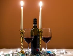 2 clear wine glass with red liquid and 2 white tapper candle thumbnail