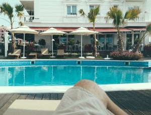 person in white shorts lying on outdoor lounge chair in front in ground pool during daytime thumbnail