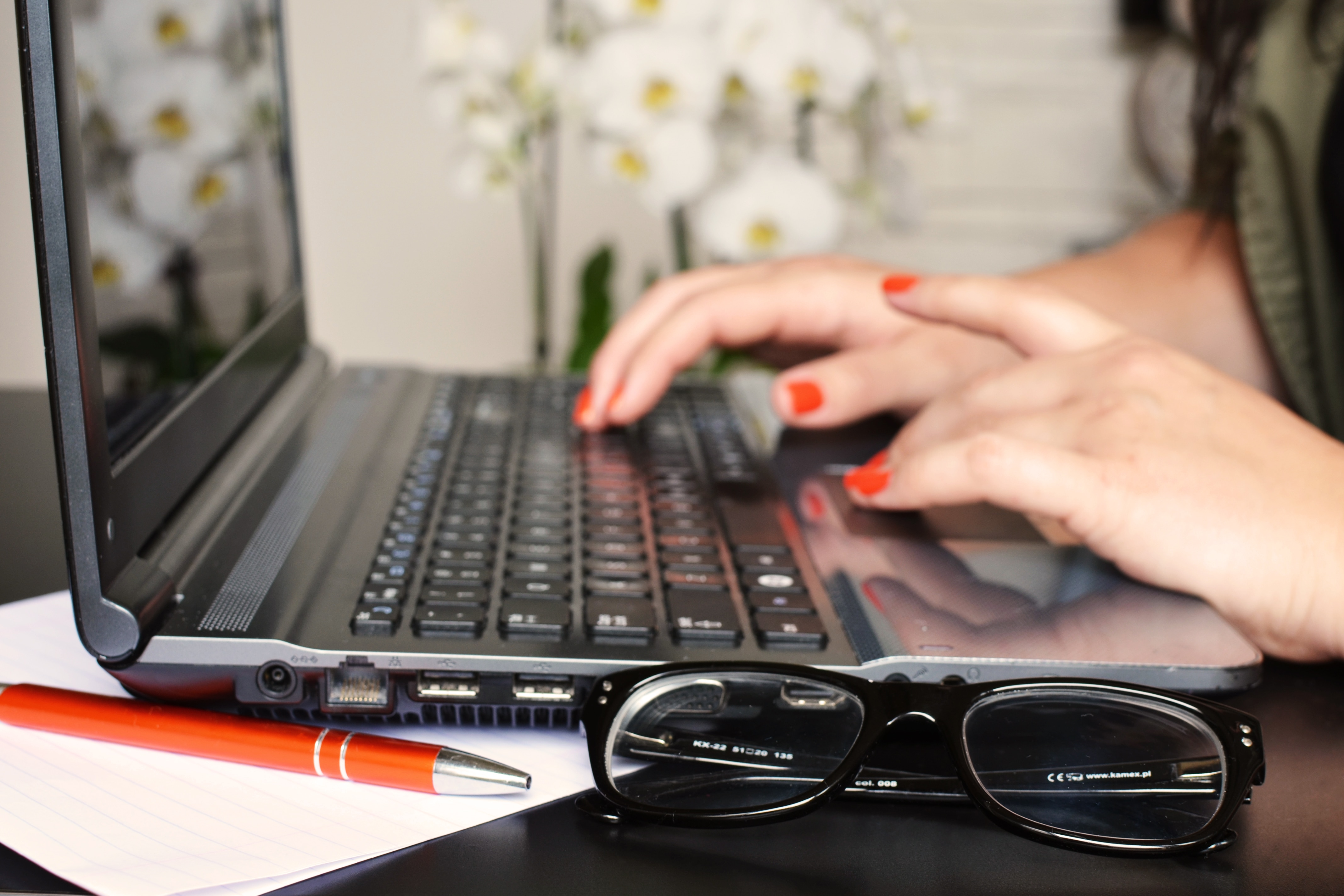 woman in orange manicure typing on black laptop