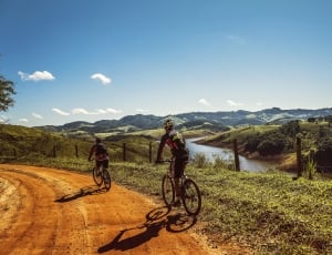 two person riding bicycles on the road with green hills background thumbnail