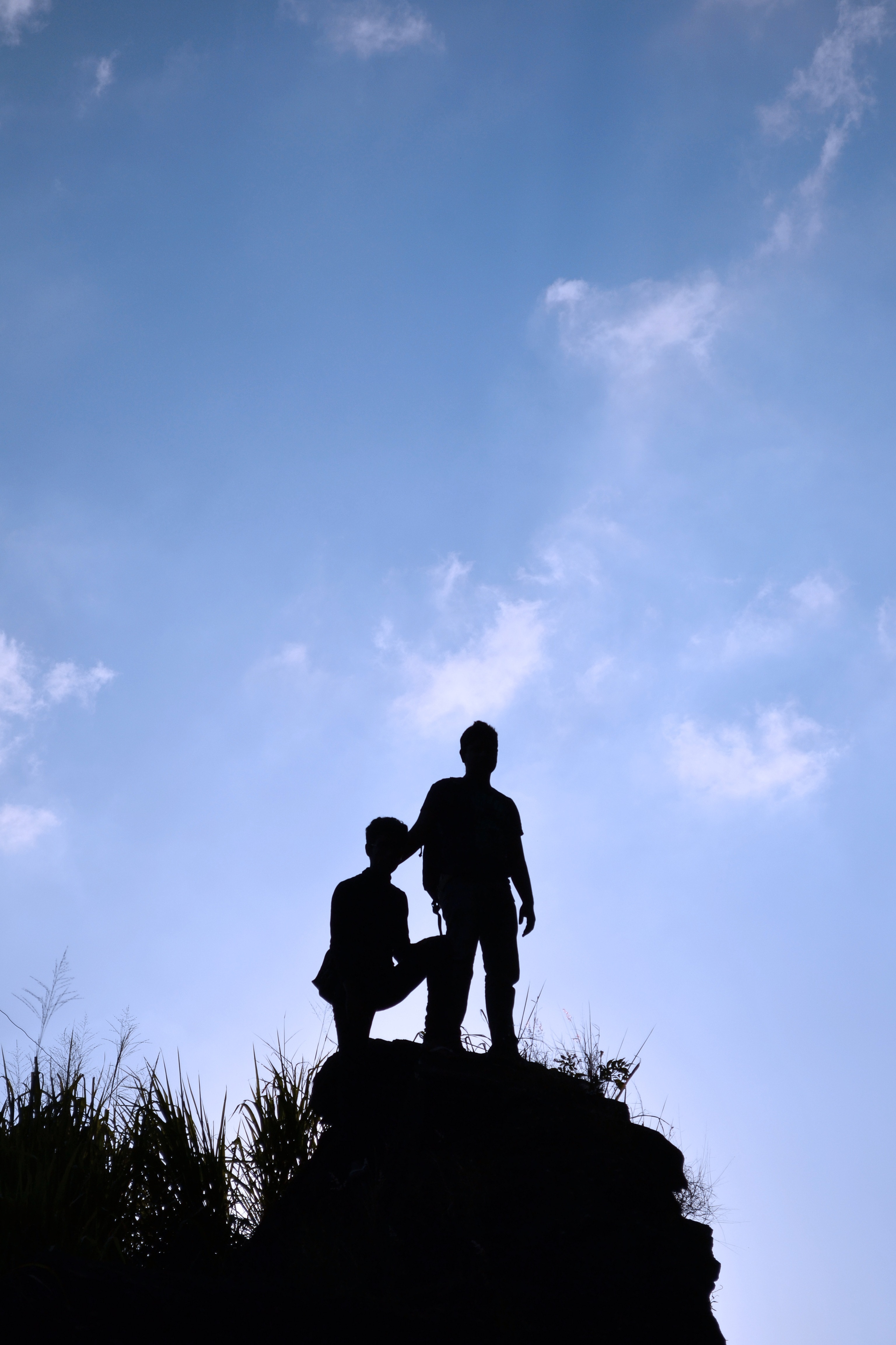silhouette of 2 man on top of rock