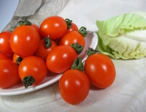 orange tomatoes on white ceramic plate near cabbage on white table thumbnail