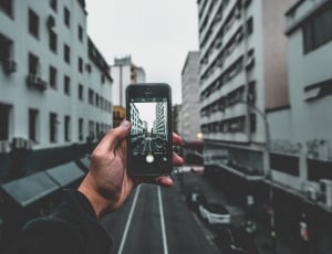 person holding black smartphone taking photo of city buildings during daytime thumbnail