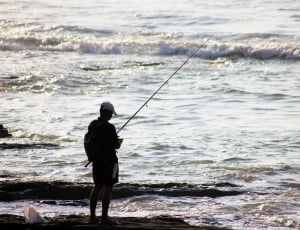man fishing by the seashore photo thumbnail