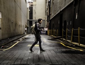 man in black walking in the middle of gray concrete thumbnail