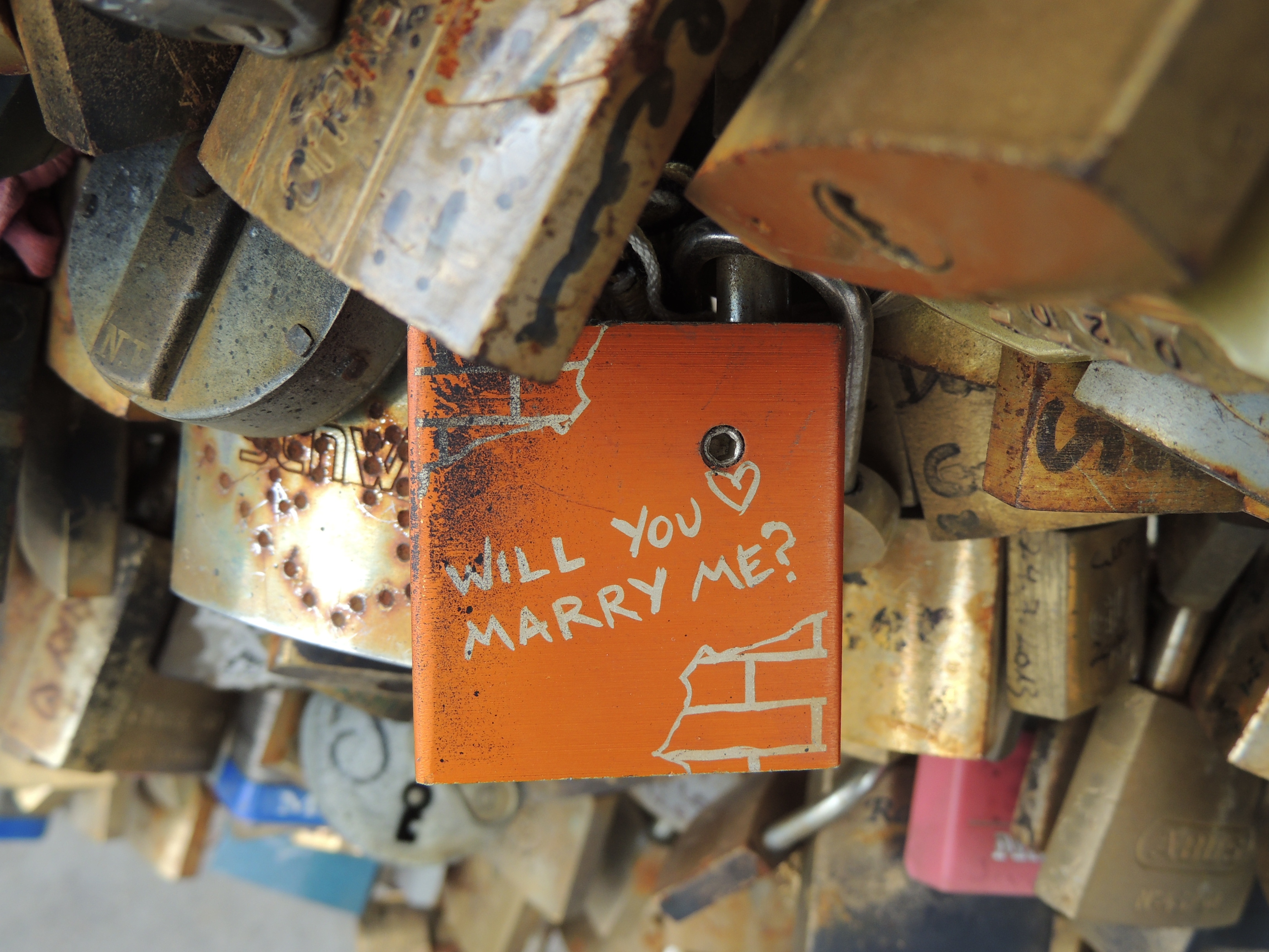 orange pad lock with will you marry me text beside lot of padlock