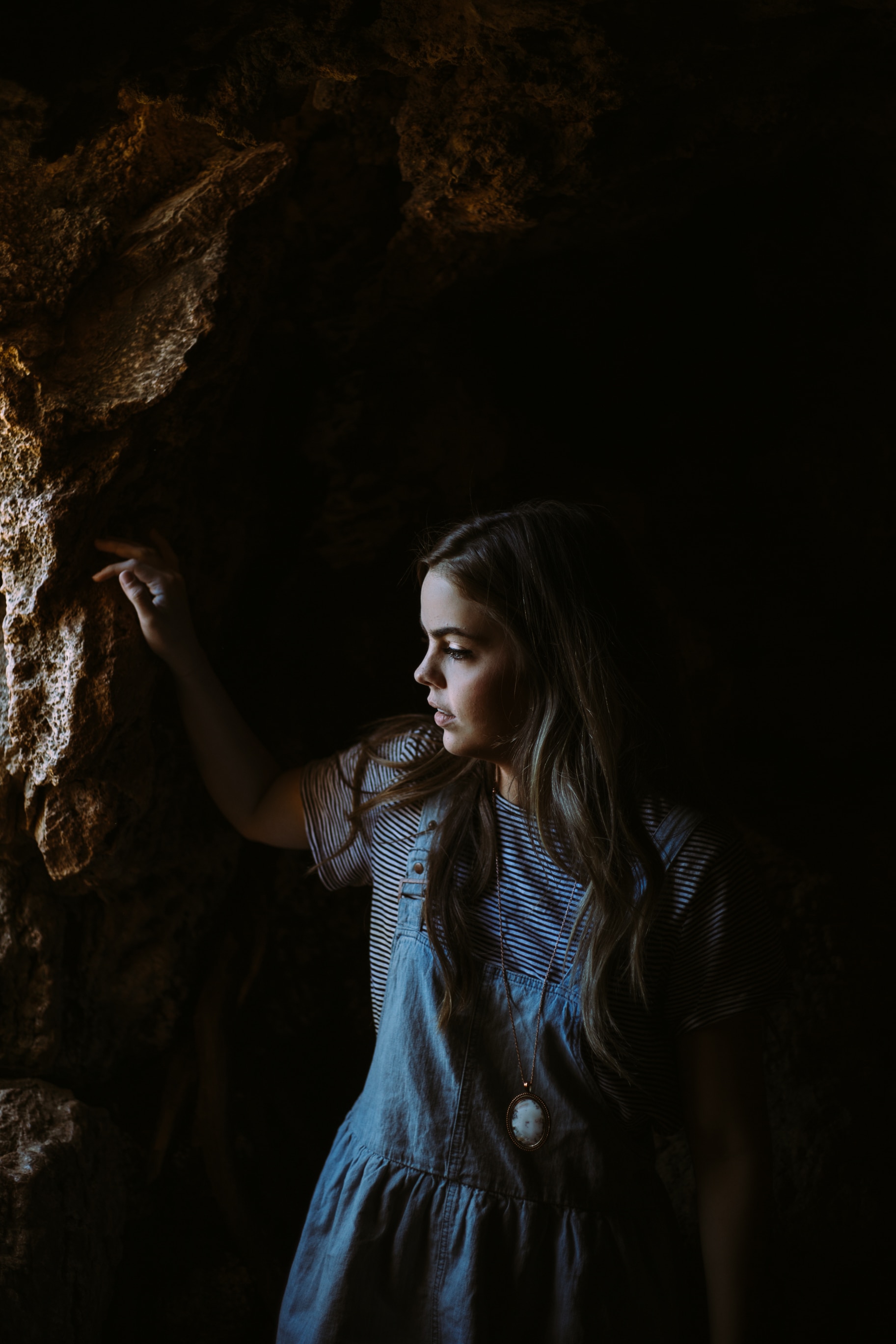 woman on blue dress wearing cameo pendant inside of the cave